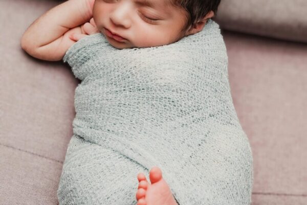 Serene newborn baby wrapped in a cozy knit blanket, peacefully sleeping indoors.